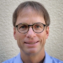 Jan Lammerding in front of a white background with black rimmed glasses and a light blue collared shirt.