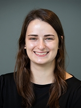 A headshot of a woman with brown hair on a gray background. 