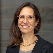 Claudia Fischbach-Teschl wearing a black blazer, smiling at the camera in front of a stone wall.