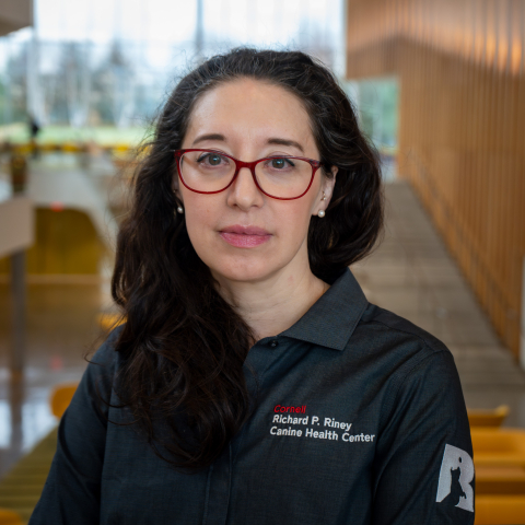 A woman with dark hair and glasses sits in the CVM atrium with a small black dog.