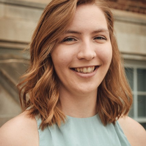 A woman with a green shirt in front of a brick wall. 