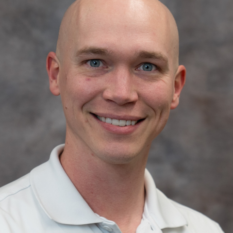 A man with blue eyes in a white shirt against a gray back drop. 