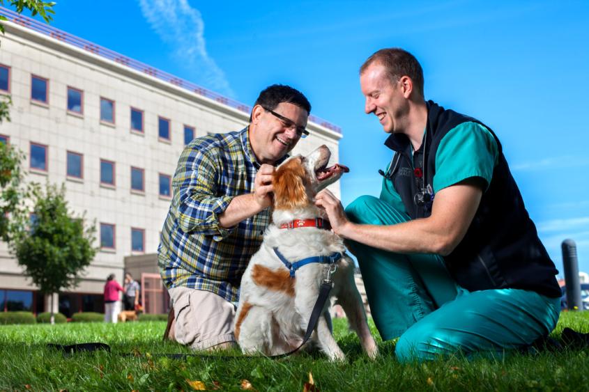 Dr. Chris Frye and male client happily pet a dog in front of Cornell's Hospital for Animals 