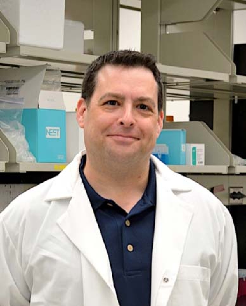 Andrew White wearing a lab coat and a navy blue shirt, standing in the lab.