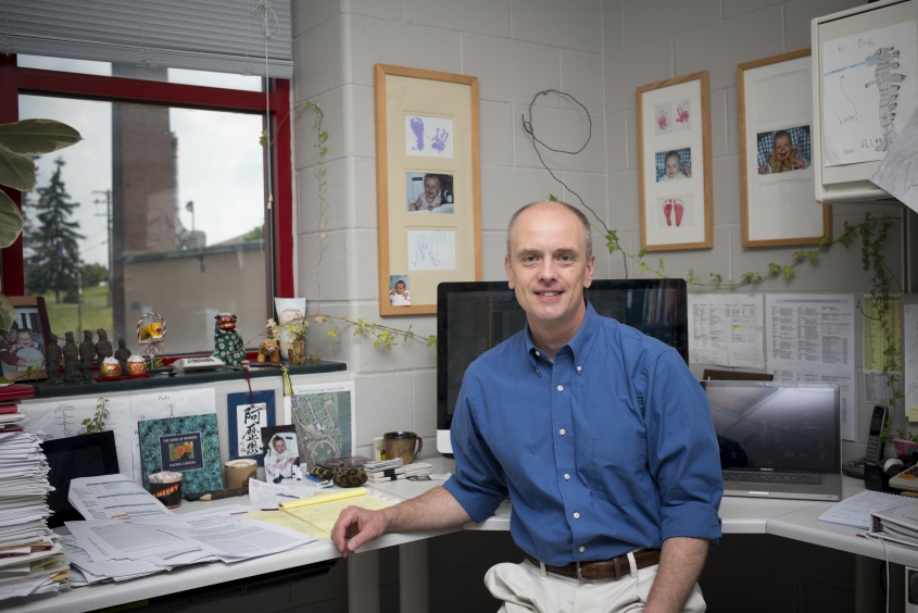 A man sitting at a desk wearing a blue button up shirt.