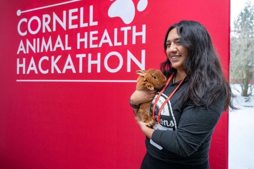 Student holding rabbit in front of hackathon banner