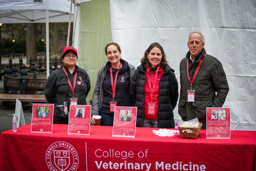Four veterinarians stand behind a red table cloth with name signs. 