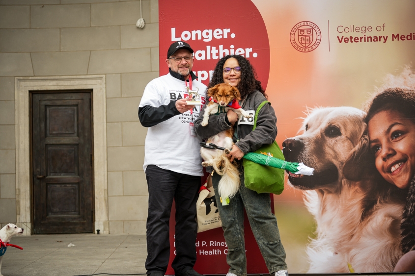 A man, woman and dog stand on stage for an award photo.