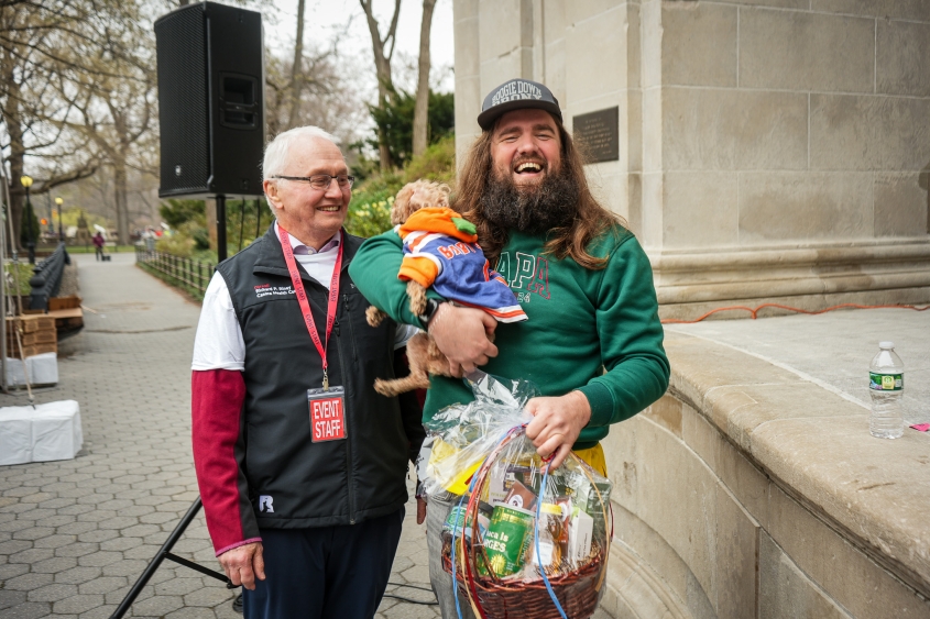 Two men stand with a dog and a gift basket. 