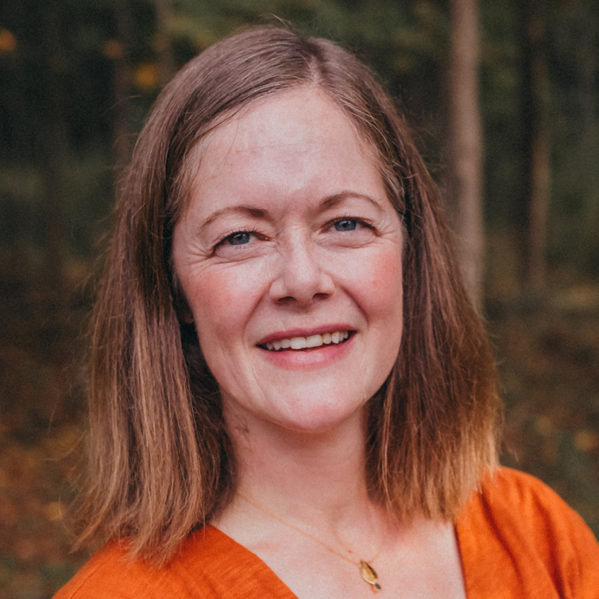 Katie Fiorella wearing an orange blouse in the woods.