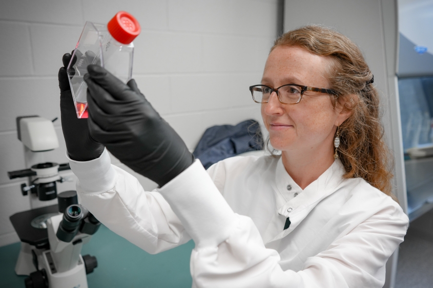 A red haired scientist looks into a container with pink liquid at Baker. 