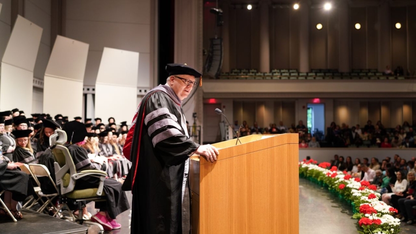 Dean Warnick at podium at hooding ceremony