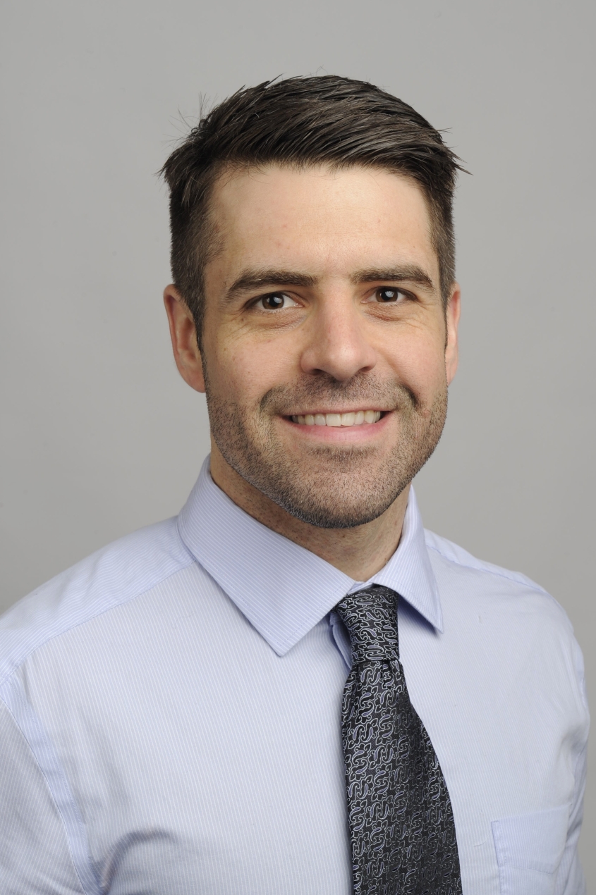Portrait photograph of Dr. Stephen Hatfield smiling in front of a gray background.