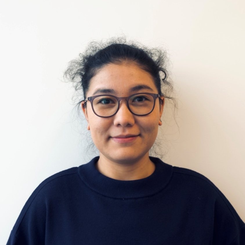 Portrait photograph of Dr. Munisha Muminingjiang smiling in front of an off-white background.