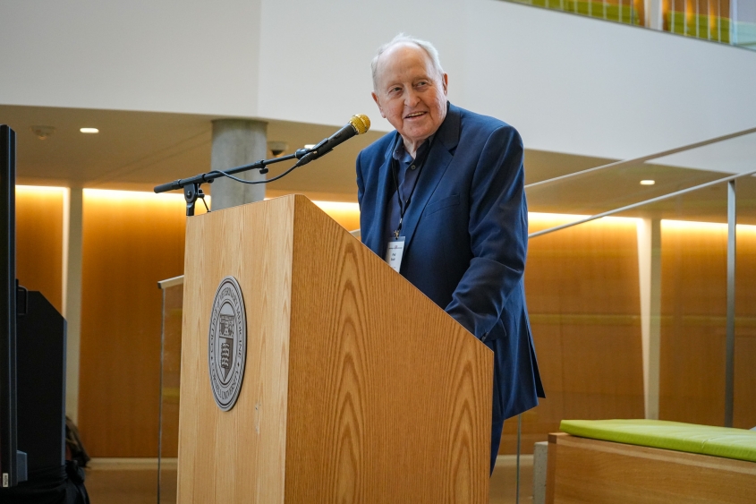 A man in a blue cat stands at a podium smiling. 