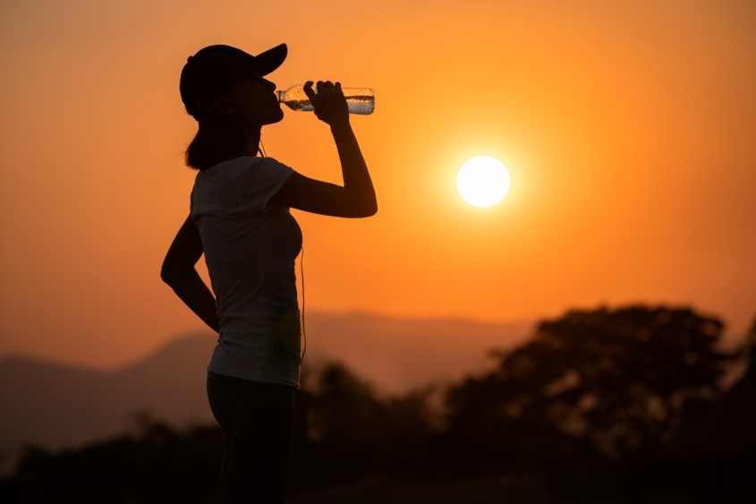 A woman drinking from a water bottle in front of the sun