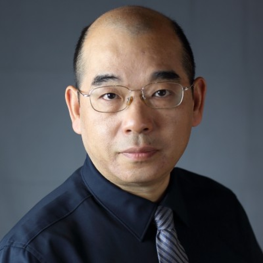 Shu-Bing Qian wearing a black collared shirt and a light purple tie with navy blue stripes.