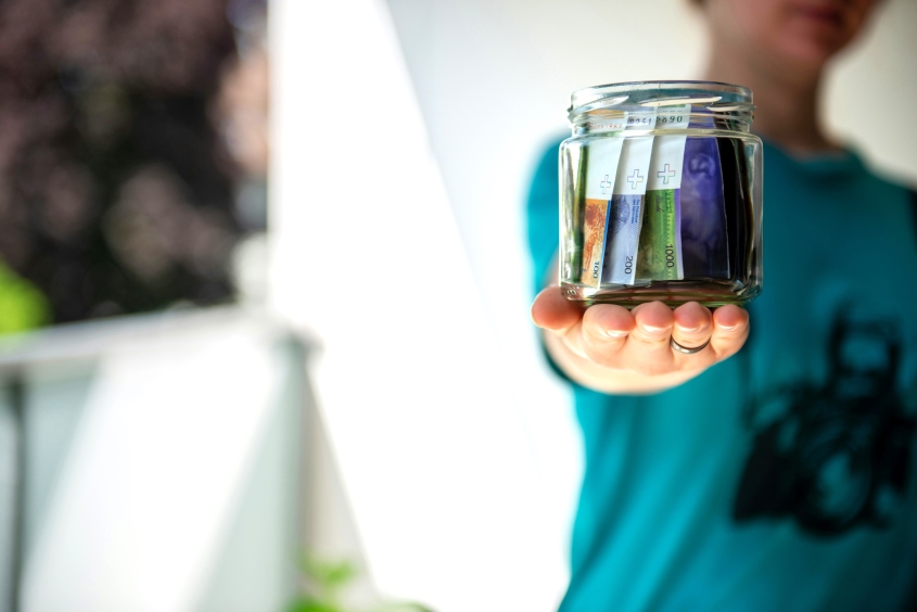 a person extending their hand holding a jar containing money