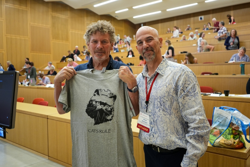 Two men stand inside one of the CVM lecture halls with a gray shirt that says "Cat's Rule."