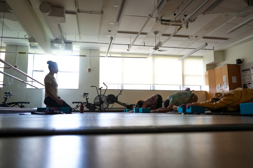 A woman sits at the front of the Wellness Room at CVM leading a yoga session. 