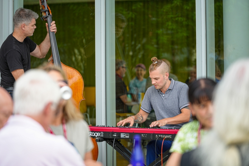 A man plays the keyboard while another plays the standing bass outside the CVM atrium during a BBQ. 
