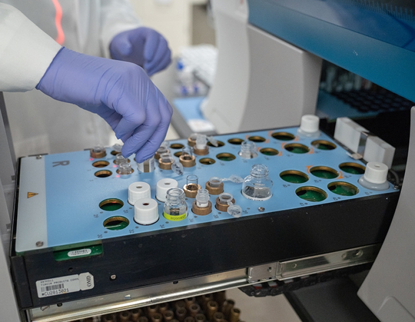 Gloved hands place a sample tube into machinery in the coagulation lab