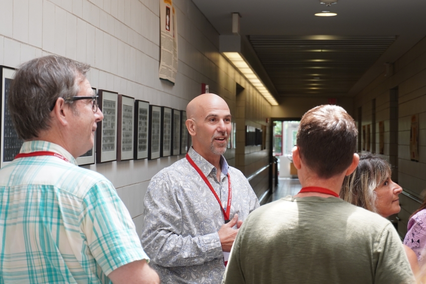A bald man with a goatee leads a group down a hallway with portraits hung on the sides. 