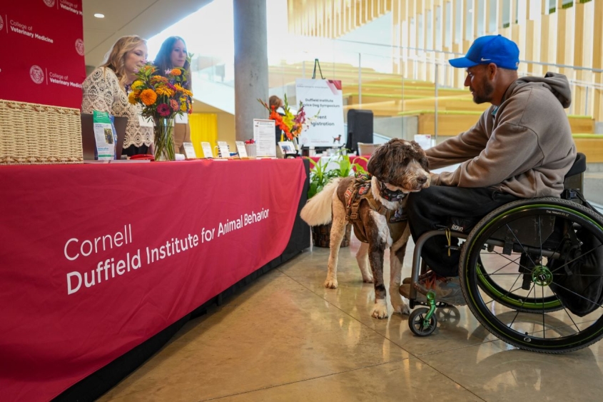 Man in wheelchair with service dog at duffield symposium welcome table