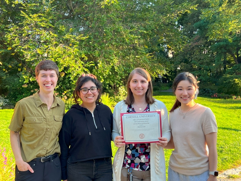 Four people standing together in front of trees. 