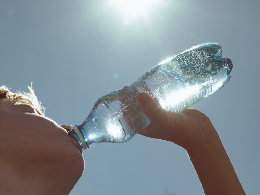 A boy drinking from a water bottle under a bright sun