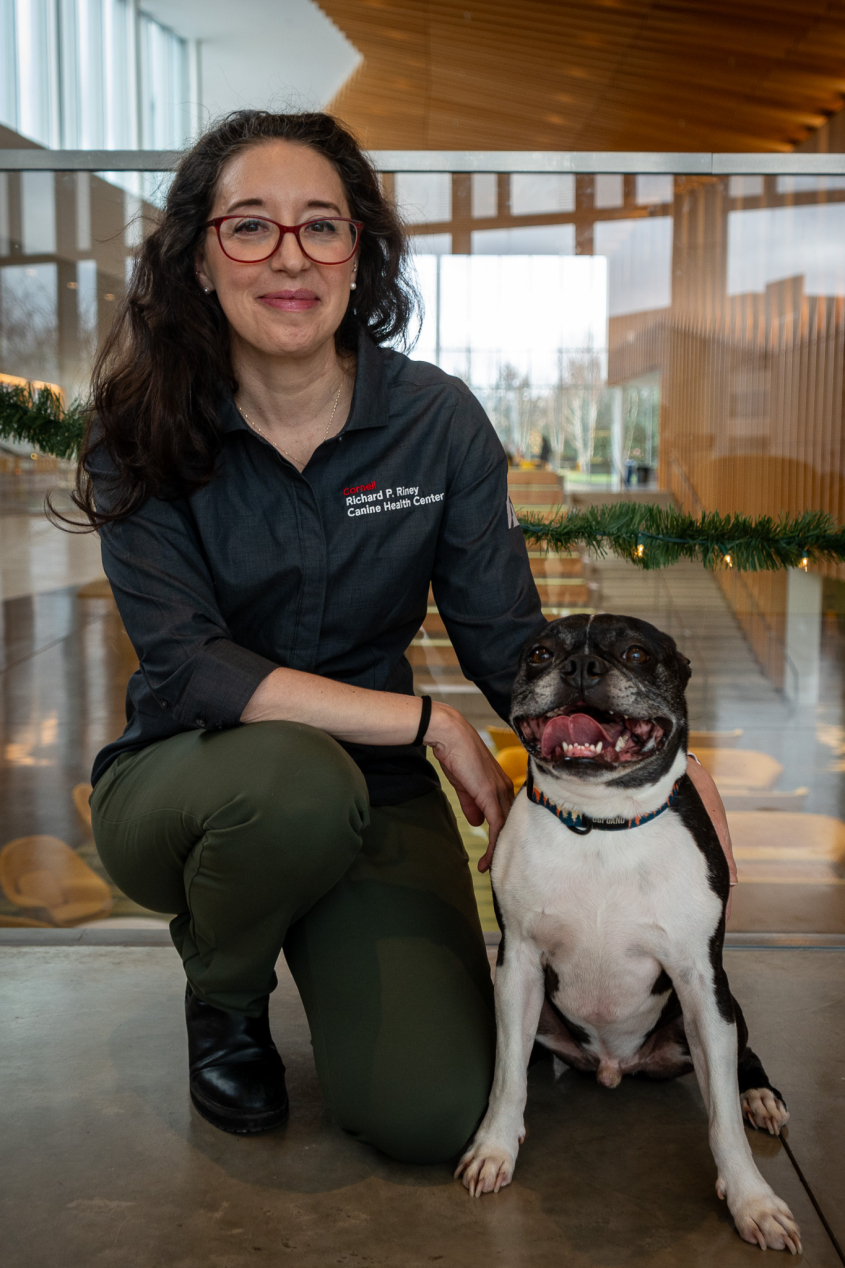 A woman with dark hair and glasses sits in the CVM atrium with a small black dog.