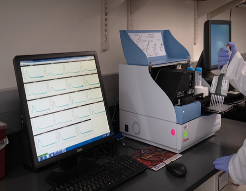 Close up of a monitor displaying results while a gloved hand handles a sample