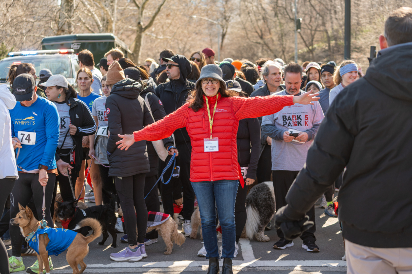 A woman wearing a red jacket stands in front of a crowd of people. 