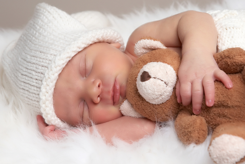 A newborn asleep hugging a teddy bear