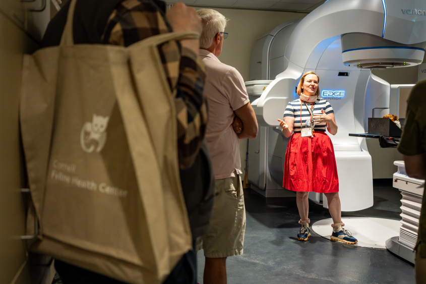 A woman stands in front of a medical machine speaking to a crowd. 