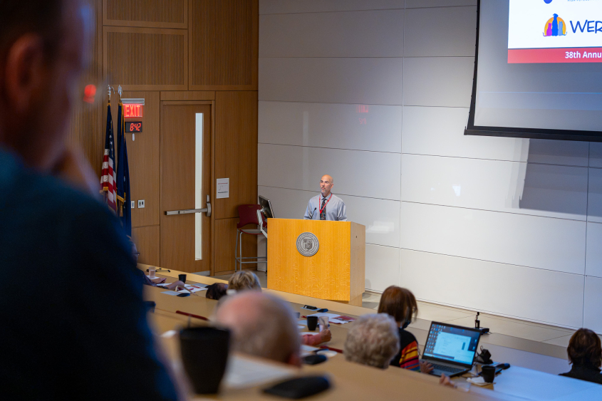 A man stands at the podium inside the lecture hall of CVM. 
