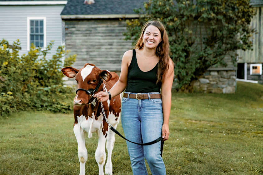 Alexandria Henderson leading a cow in front of a farm