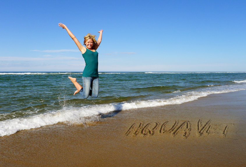 A woman jumping on a beach with the word AQUAVET written in the sand