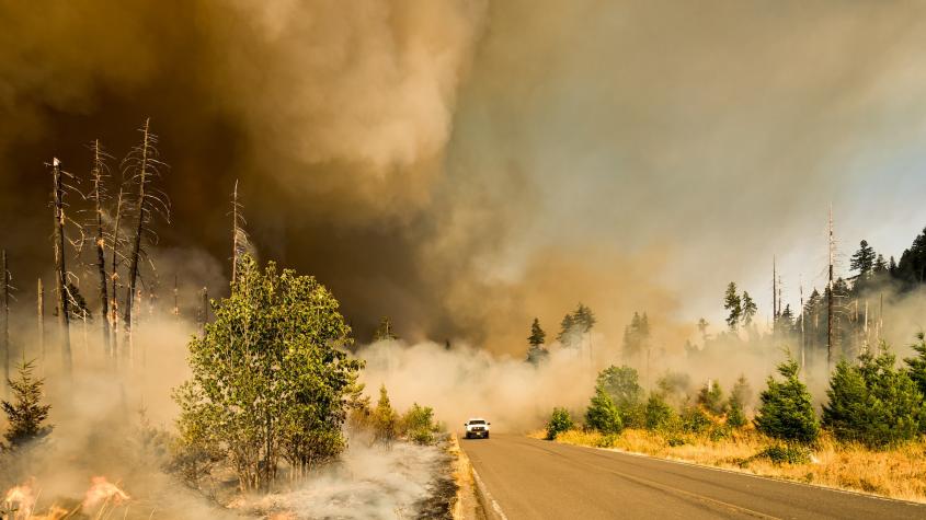 A car driving away from a smoke caused by a wildfire 