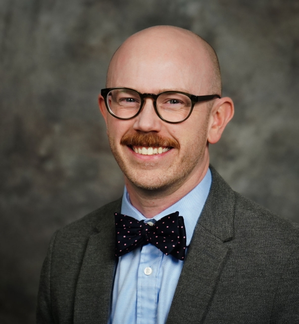 Dr. Mason Jager wearing a gray blazer, light blue collared shirt, and a bow tie.