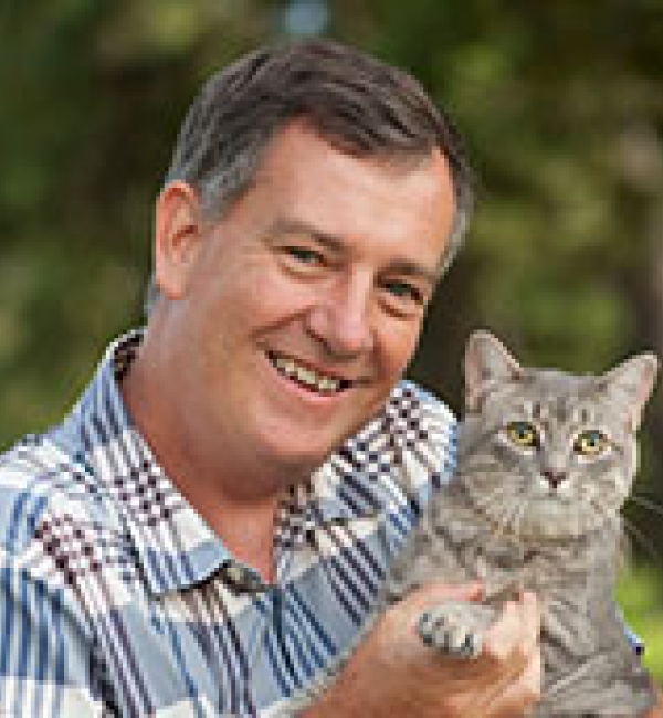 A photo of a man wearing a striped shirt holding a cat outside. 