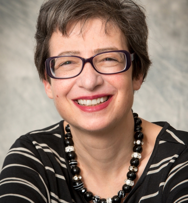 Ruth Collins working wearing black shirt with white stripes, black acrylic glasses, and necklace with large black and transparent beads.