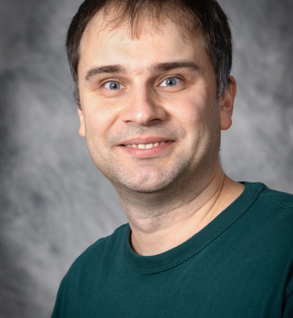 Andrew Flyak in a gray background wearing a turquoise green shirt.