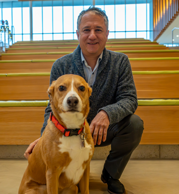 A man with gray sweater stands with a dog. 