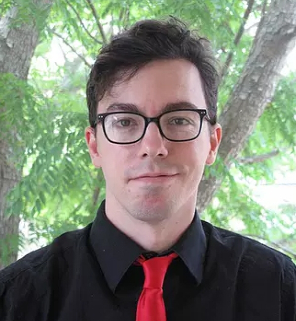 Portrait photograph of Dr. Brandon Hedrick smiling in front of a background of trees