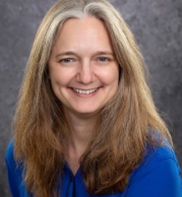 Portrait photograph of Dr. Kelly Hume smiling at the camera in front of a dark gray background