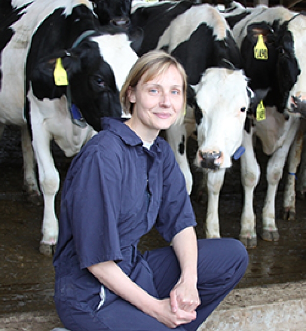 Sabine Mann in a navy-blue jumpsuit in front of at least three cows.