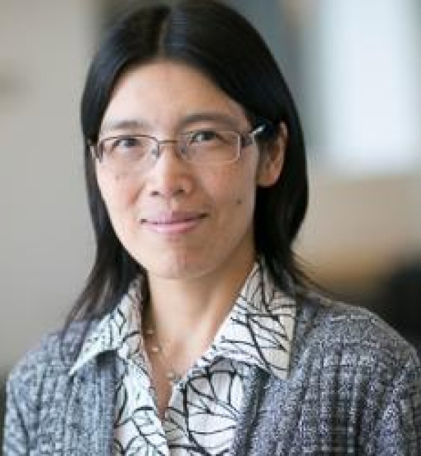 Fenghua Hu wearing thin-framed metallic glasses, a knitted gray blazer and a white collared shirt with Black-lined patterns.