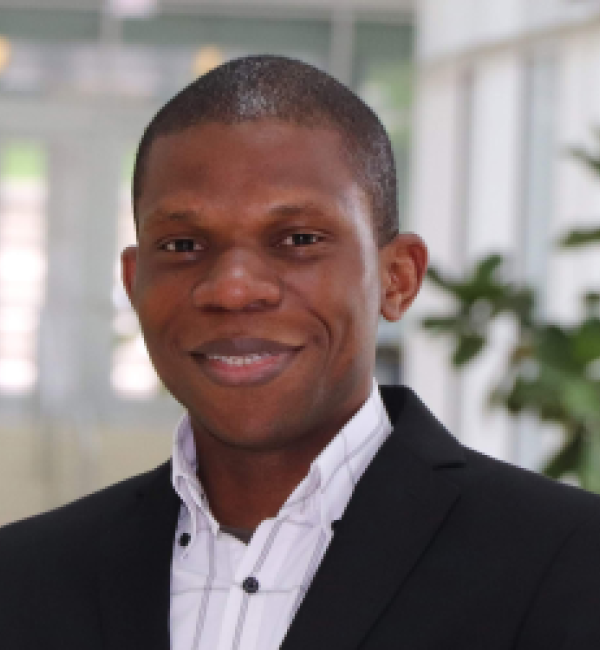 Zeribe Nwosu in a black blazer and white collared shirt with grey squares behind an entrance.