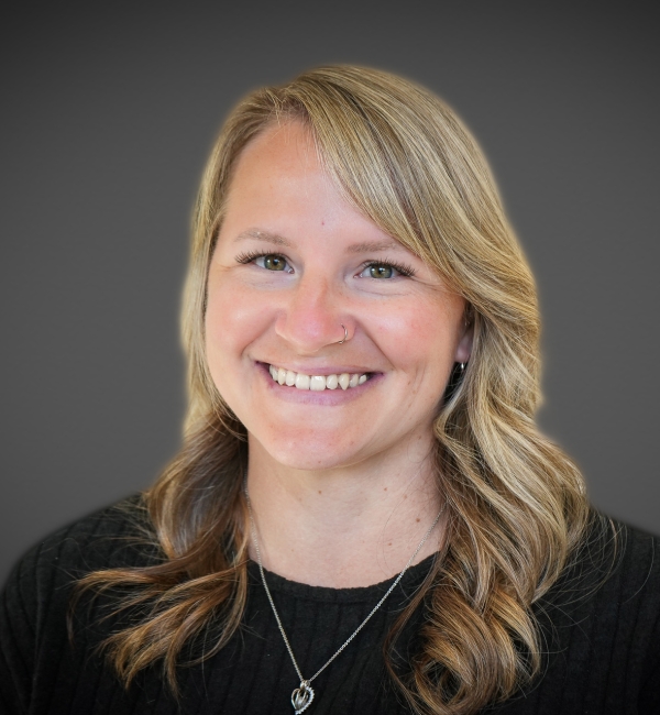 A headshot of a woman with blonde hair on a gray background. 